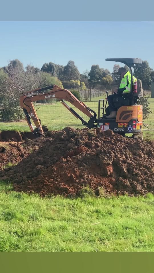 Mini excavator digging and moving soil on a suburban lawn